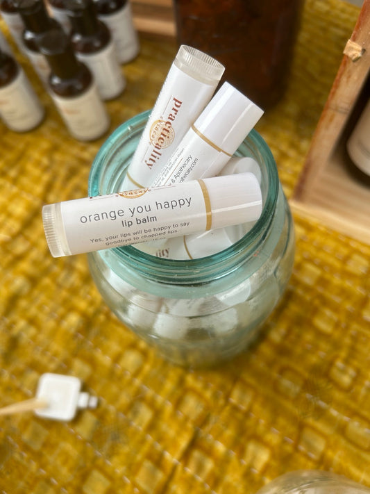 Practicality Orange You Happy Lip Balm tubes displayed in a glass jar at the shop
